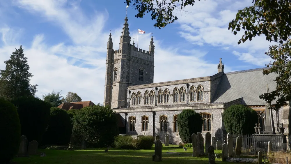 St Mary and all saints church sunny day with an st george's cross flag flying on top and a grave yard in front
